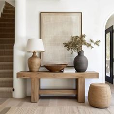 a wooden table with two vases and a lamp on it in front of a staircase