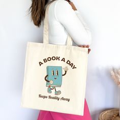 "Introducing our whimsical canvas tote bag, adorned with a charming vintage book mascot cartoon and the delightful slogan \"A book a day keeps reality away.\" Crafted for book lovers who appreciate both style and wit, this sturdy tote is perfect for carrying your literary essentials with a touch of literary charm. Embrace your love for reading and make a statement wherever you go! 📚 This 100% cotton bag comes in one size - 15\" x 16\"- perfect for everyday wear. The bag features 20\" handles (made from the same canvas), making it easy to carry even with a week's worth of shopping. .: 100% cotton canvas .: Heavy fabric (12 oz/yd² (406.9 g/m .: Sewn-in label" Vintage Rectangular Canvas Bag As Gift, Rectangular Canvas Bag With Bookish Style, Canvas Bag For Back To School Gift, Bookish Rectangular Canvas Bag, Back To School Canvas Bag Gift, Retro Canvas Bag As A Gift, Bookish Bags With Letter Print For Gift, Gifts For Book Lovers, Book Bags