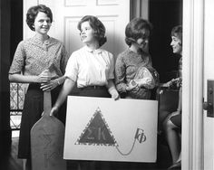 three women holding up a cardboard sign with the letters k and p on it while standing in front of a door