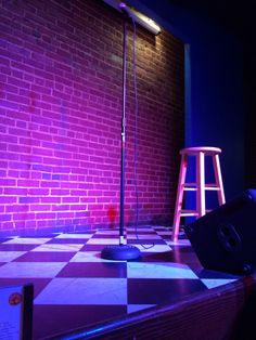 a purple light shines on the floor in front of a red brick wall and stool