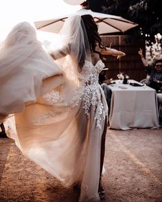 a woman in a wedding dress is dancing with an umbrella over her head and people sitting at tables behind her