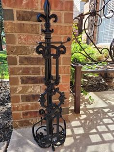 a tall black metal plant stand next to a brick wall in front of a house