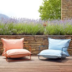 two chairs sitting on top of a wooden deck next to a wall covered in plants