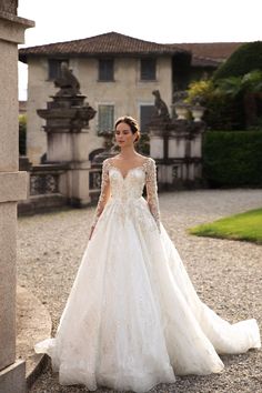 a woman in a white wedding dress standing on the ground near a stone wall and building