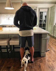 a man standing next to a dog on top of a hard wood floor in a kitchen