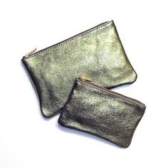 two metallic purses sitting next to each other on a white surface and one has a gold zipper