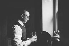 black and white photograph of a man holding a glass in front of a window looking out the window