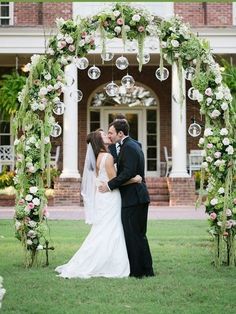 a bride and groom kissing under an outdoor wedding arch