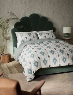 a bed with green headboard and pillows next to a plant in a room filled with furniture