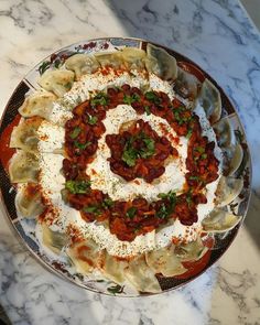 a plate filled with dumplings covered in sauce and toppings on top of a marble table