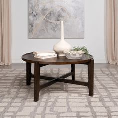 a coffee table with a vase and books on it in front of a large painting