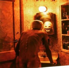 a man standing in front of a bathroom mirror looking at himself in the mirror with an evil mask on his head