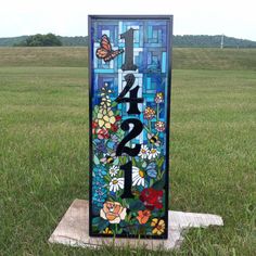 a stained glass sign with flowers and butterflies on it in the grass next to a field