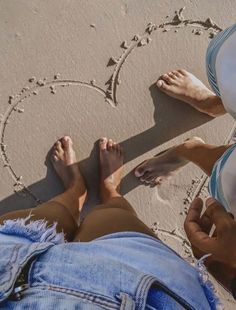 two people sitting on the beach with their feet in the sand making a heart shape