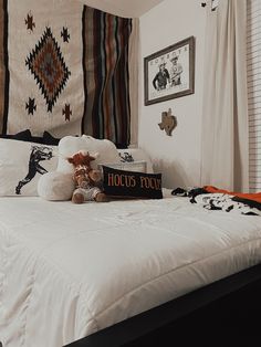 a bed with white sheets and pillows in a bedroom next to a wall hanging on the wall