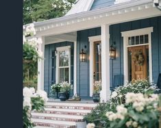 a blue house with white trim and flowers on the front porch, along with potted plants