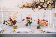 the table is set with white plates, goldware and floral centerpieces on it