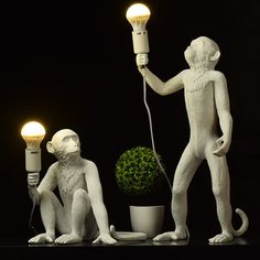 two white statues holding light bulbs next to a potted plant