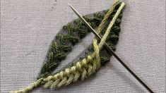 two crochet needles are next to each other on a piece of fabric with green and white yarn