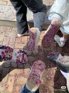 several people standing on the sidewalk with their feet covered in pink confetti petals