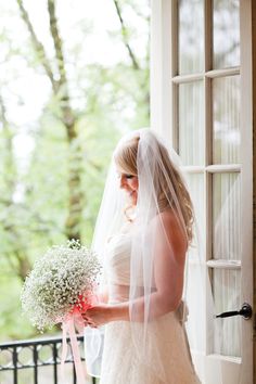 a woman in a wedding dress is holding a bouquet and looking out the window at something