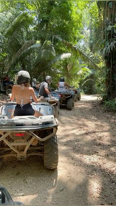 several people riding four wheelers in the jungle on dirt road with trees and bushes