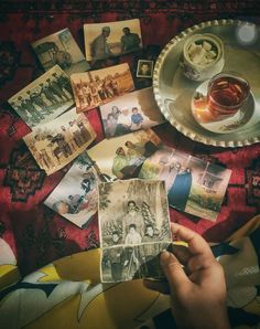 a person holding up some old photos next to a plate with tea and other items on it