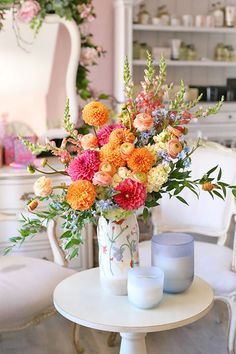 an arrangement of flowers in a white vase on a table with candles and other decorations