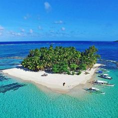 an island in the middle of some water with boats parked on it and palm trees