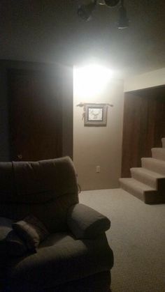 an empty living room with stairs leading up to the ceiling and a recliner chair