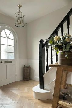 a vase with flowers sitting on top of a wooden table next to a stair case