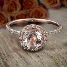 an oval shaped morganite and diamond ring on a wooden surface with roses in the background