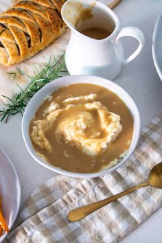 a bowl of mashed potatoes and gravy on a table next to bread