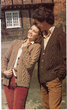 two people standing next to each other in front of a brick building and one person is wearing a sweater