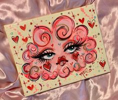 a painting with hearts and eyes on a pink satin surface next to a pink sheet