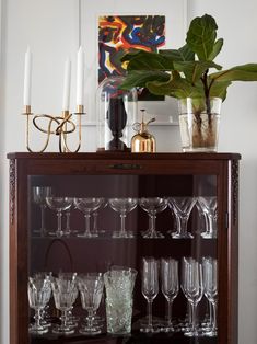 a display case filled with lots of wine glasses and candles next to a potted plant