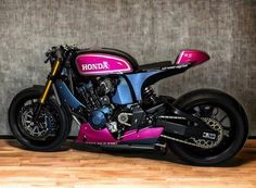 a pink and blue motorcycle parked on top of a hard wood floor next to a wall