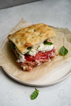 a sandwich with meat, cheese and vegetables on a white plate next to some leafy greens