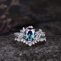 a blue and white diamond ring sitting on top of a black stone covered ground with leaves