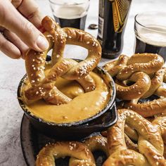 pretzels being dipped with caramel sauce in front of beer mugs on a table