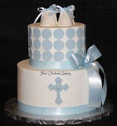 a three tiered cake decorated with blue and white polka dots, bows and a cross