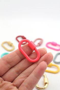 a hand holding a small plastic object in it's palm with several different colored paper clips around it