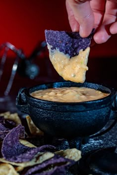 a hand dipping a tortilla chip into a bowl filled with dip and chips