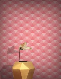 a gold vase sitting on top of a wooden table next to a pink and white wall