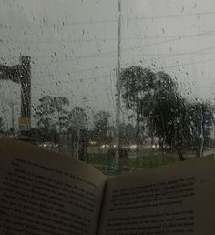 an open book sitting on top of a window sill next to rain covered windows