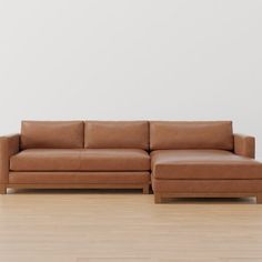 a brown leather couch sitting on top of a hard wood floor next to a white wall