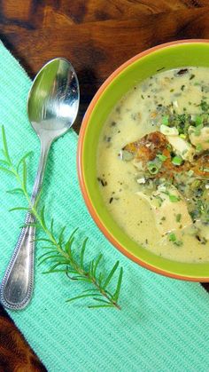 a green bowl filled with soup on top of a blue napkin next to silverware