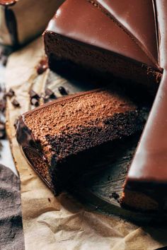 a chocolate cake is cut into slices and sitting on wax paper next to a cup of coffee