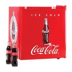 two bottles of coca cola sitting next to an ice cold cooler with the lid open