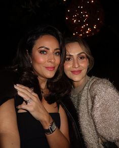 two beautiful women standing next to each other in front of a chandelier filled with lights